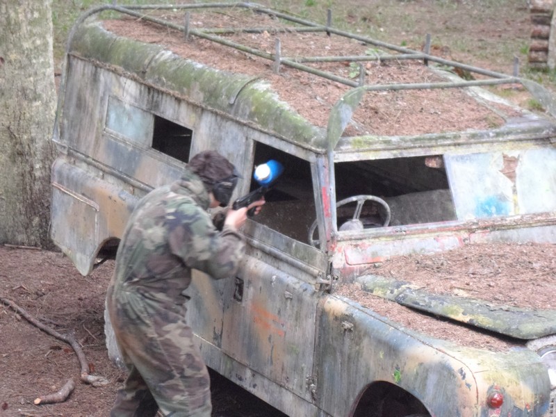 A Paintball player hiding behind a Land Rover and taking aim